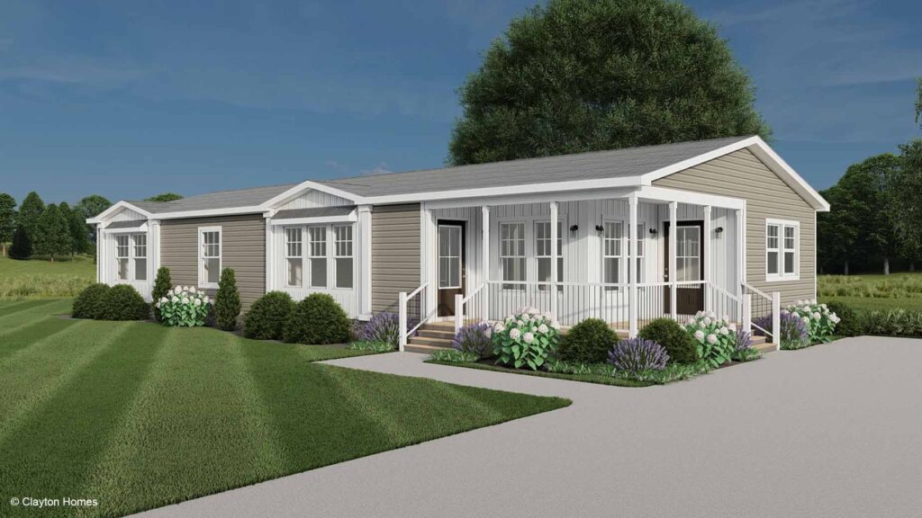 A modern manufactured home with a front porch, surrounded by bushes and a green lawn.