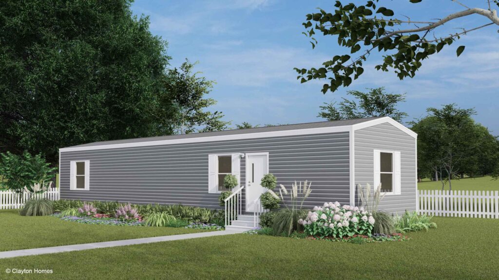 A modern gray manufactured home with white trim, surrounded by a garden and a white picket fence.