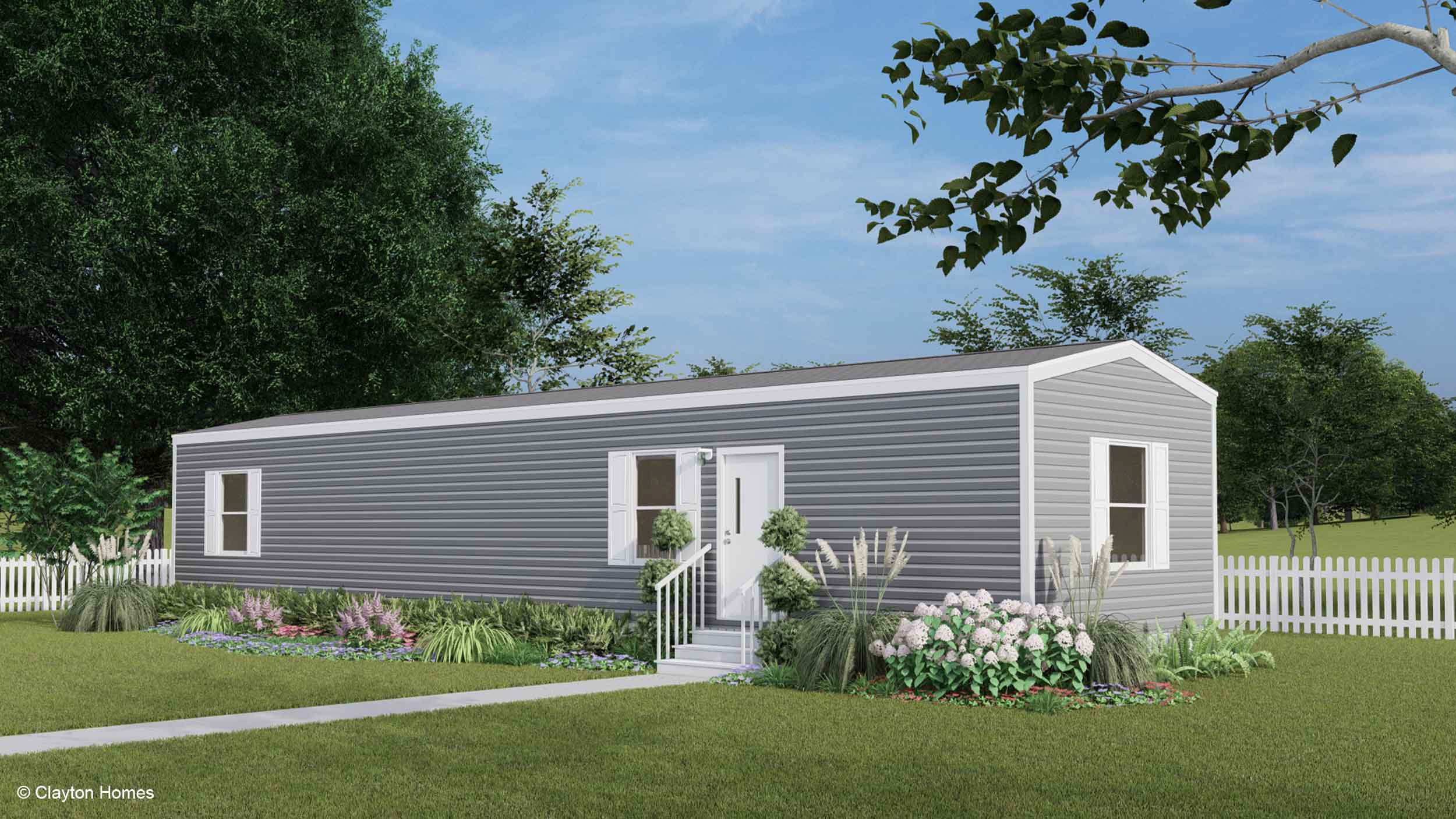 A modern gray manufactured home with white trim, surrounded by a garden and a white picket fence.