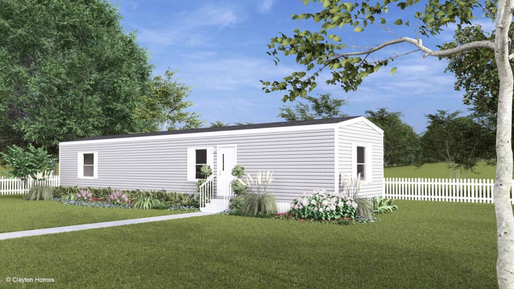 A charming white manufactured home with steps, garden beds, and a white picket fence nestled in a grassy yard.