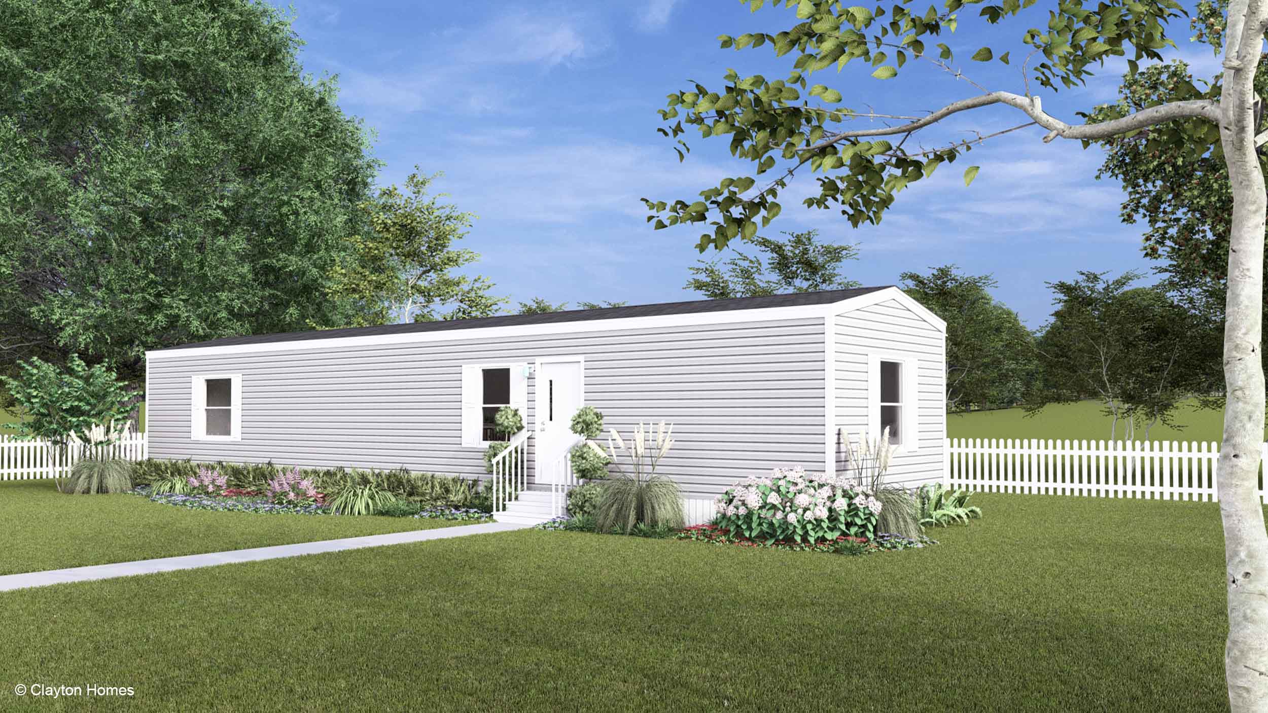 A charming white manufactured home with steps, garden beds, and a white picket fence nestled in a grassy yard.
